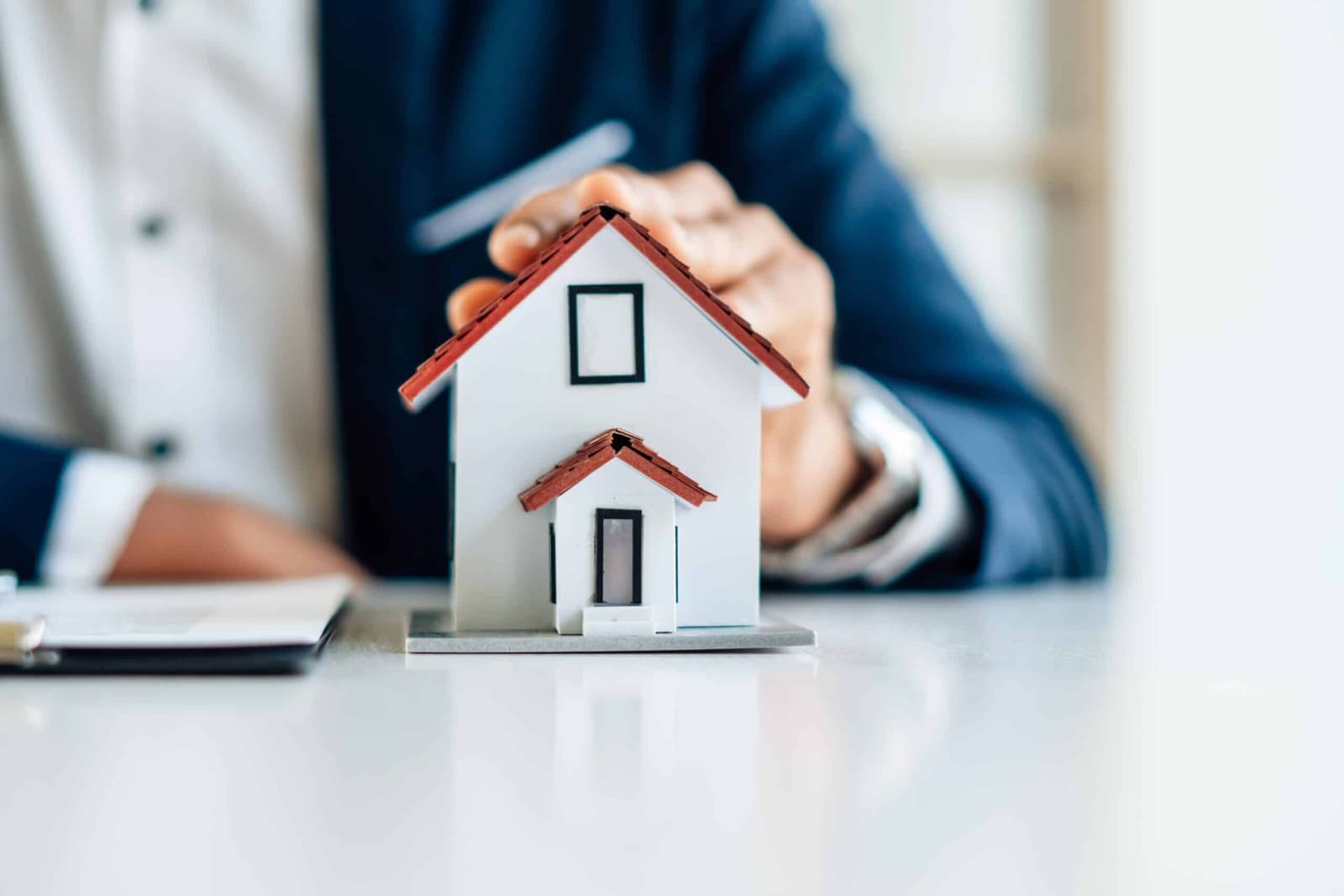 Hands sheltering a small model house on a desk