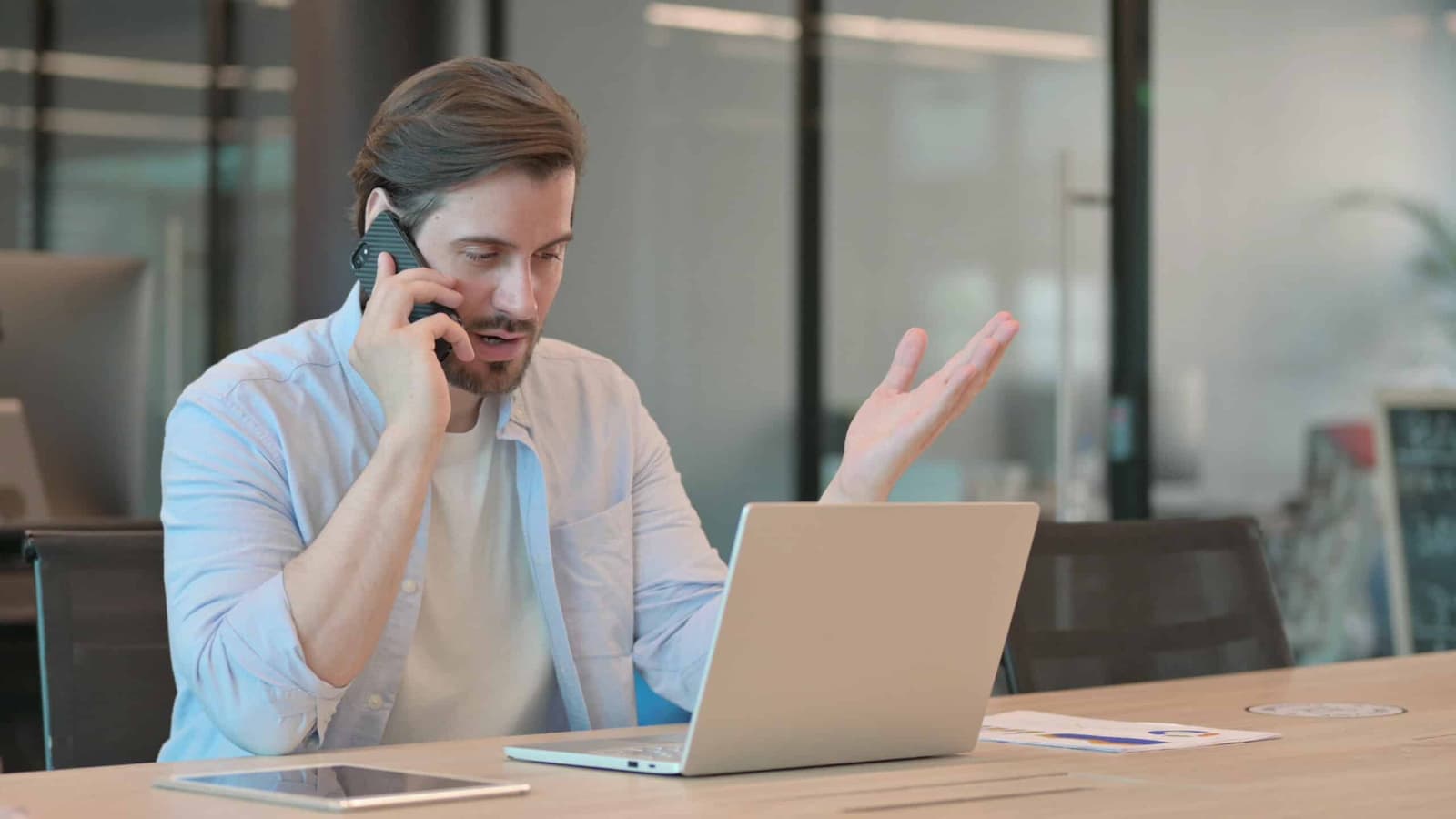 Frustrated man on the phone at a desk with a laptop