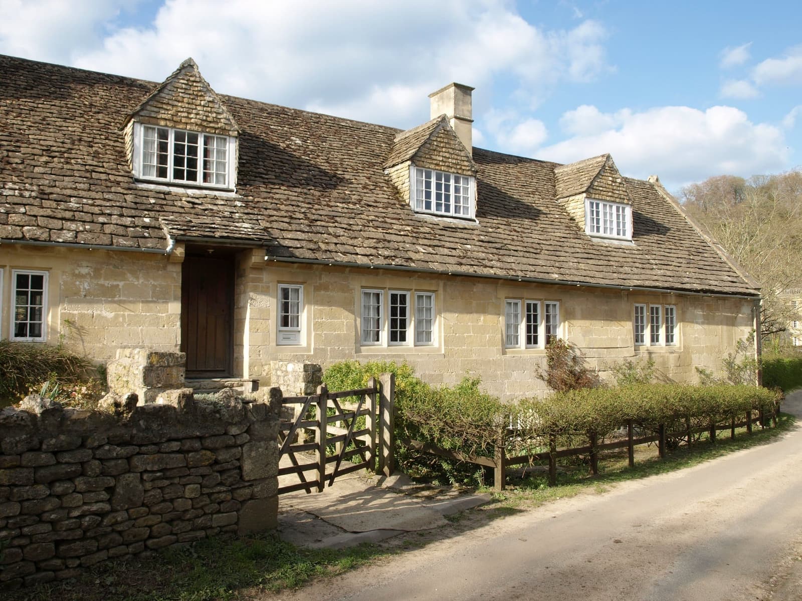 Large Cotswold stone house behind a wooden gate