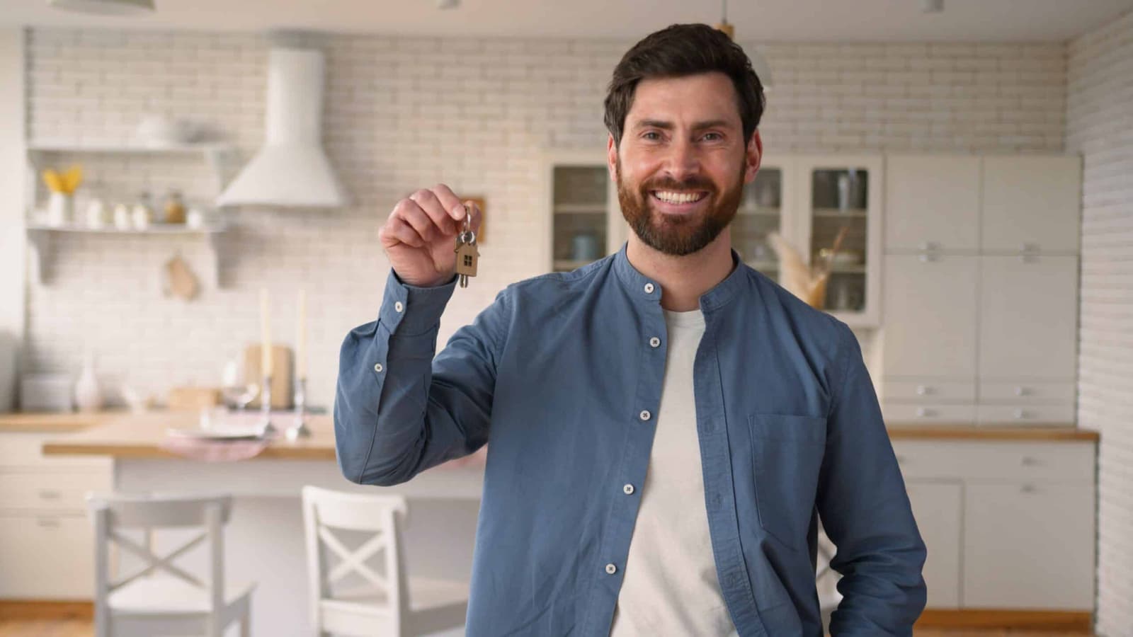Smiling man holding up keys in a kitchen