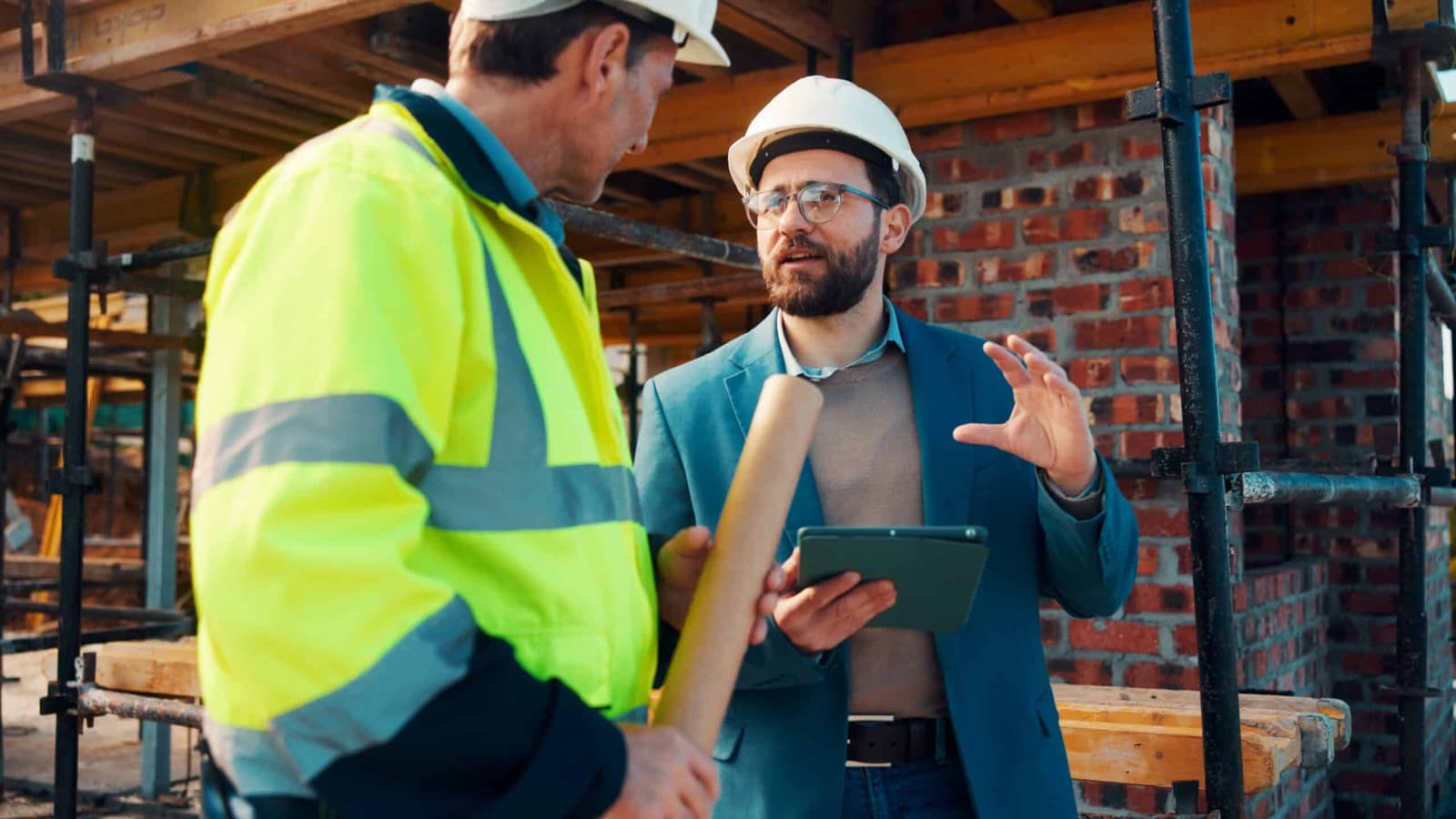 Builder in a hi vis jacket talking to a surveyor holding a tablet
