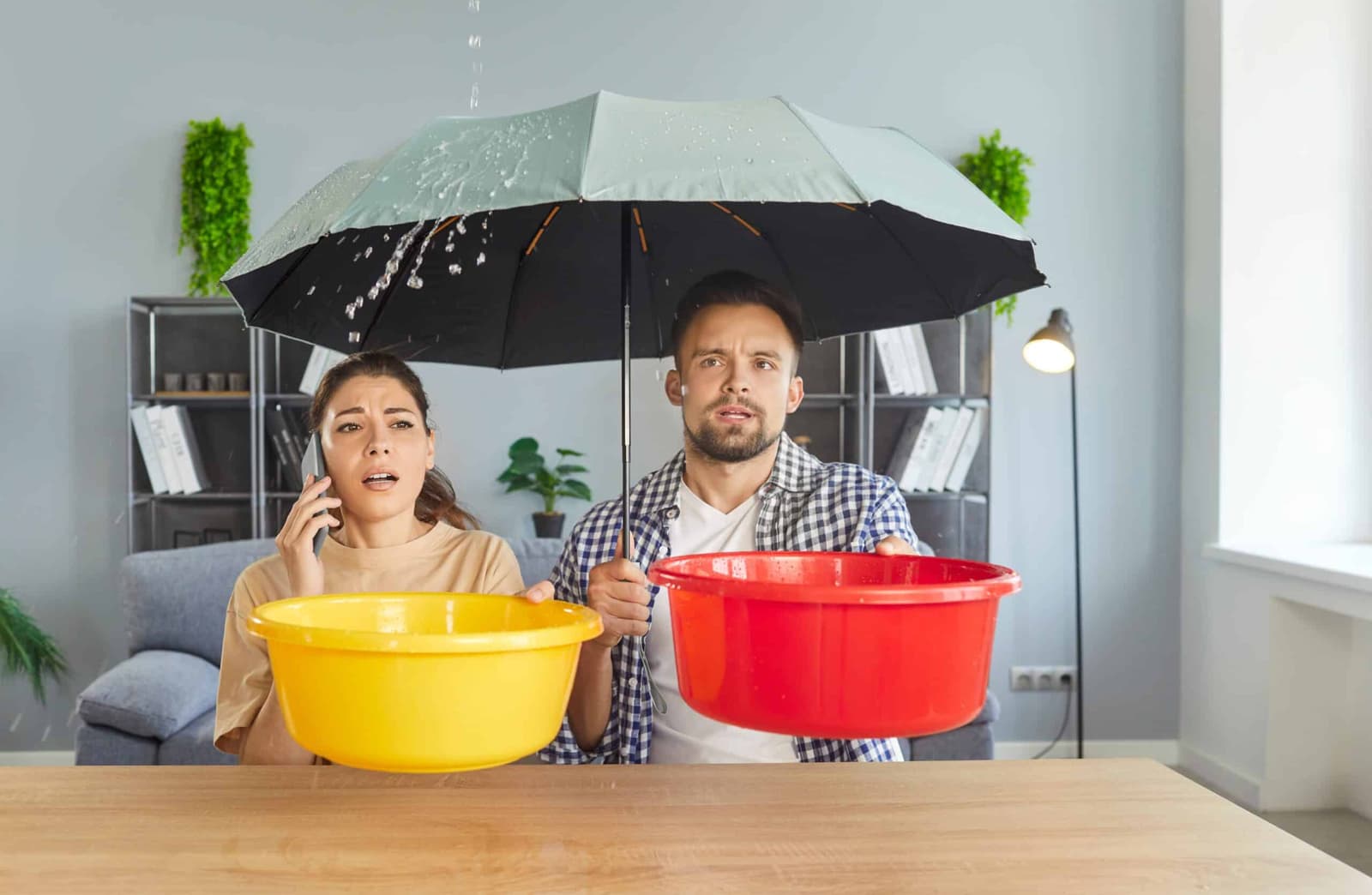 Couple sheltering under an umbrella indoors holding buckets