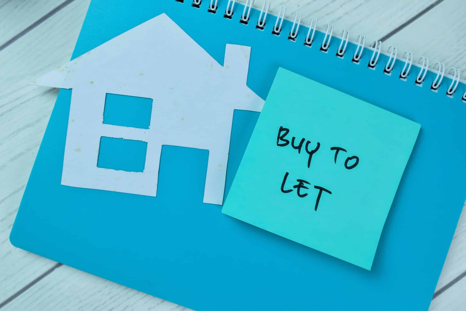 Paper house cut out beside a sticky note reading buy to let