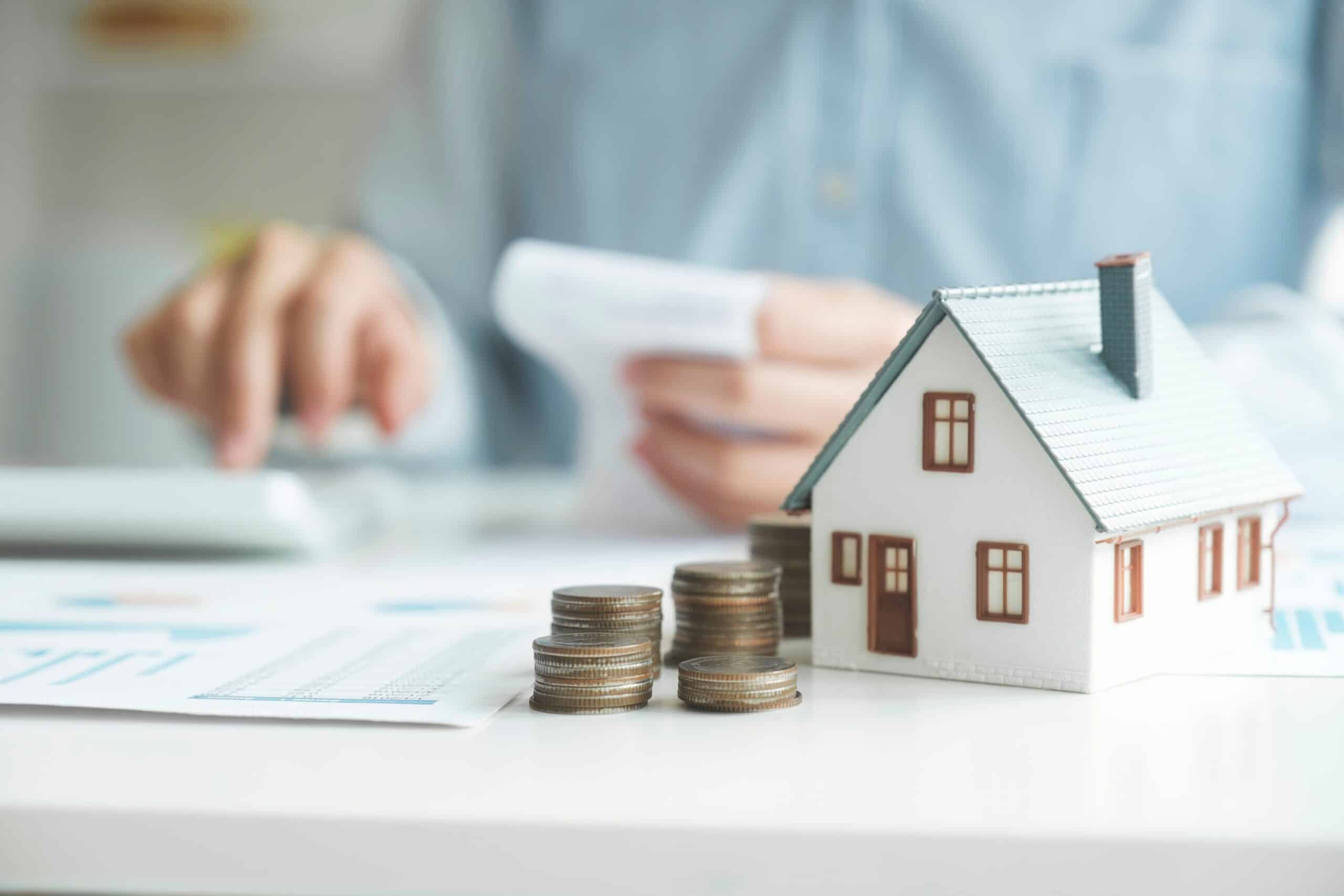 Hand with a calculator beside stacked coins and a model house
